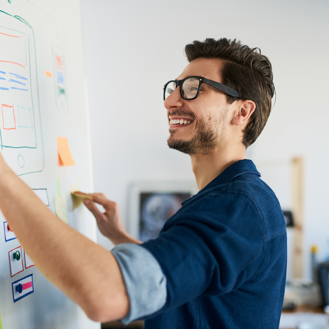 Lächelnder Mann schreibt an ein Whiteboard.